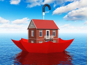 Creative real estate security, home protection and insurance business concept: residential house cottage floating in blue sea water ocean in red umbrella parasol